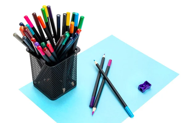 Различные цветные карандаши в чёрном металлическом офисном кубке, фиолетовая точилка и три заточенных карандаша на листе синего картона. Изолирована. Крупный план — стоковое фото