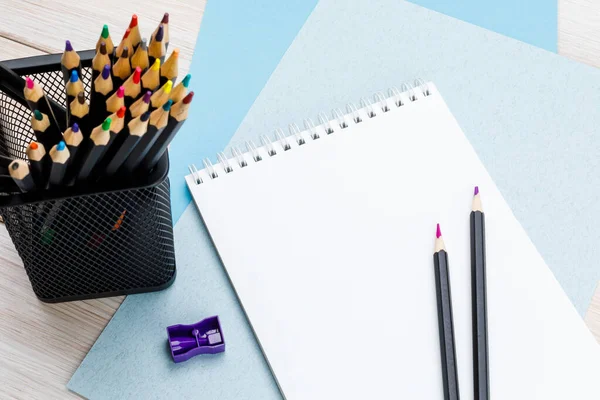 Colored pencils in a black office cup, purple pencil sharpener, a pair of sharpened pencils and a notebook on sheets of color cardboard — Stock Photo, Image