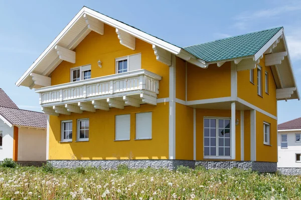 New yellow house with white windows and a large wooden balcony built in the village. — Stock Photo, Image
