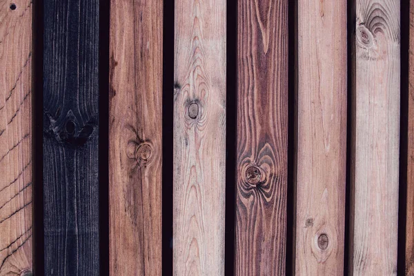 Dark wooden background. Rustic wooden fence made from treated differently colored boards. Tinted.