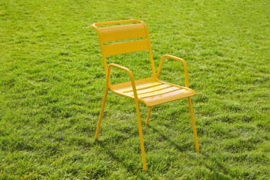 Sarı metal sandalye yeşil çimenli bir çimenlikte duruyor. Şehir teması. Yakın plan.
