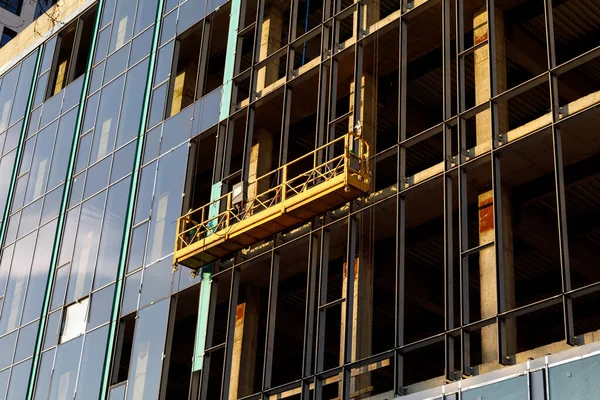 Suspended construction craddle for glazing a facade of a commercial property at sunset. Engineering urban background.