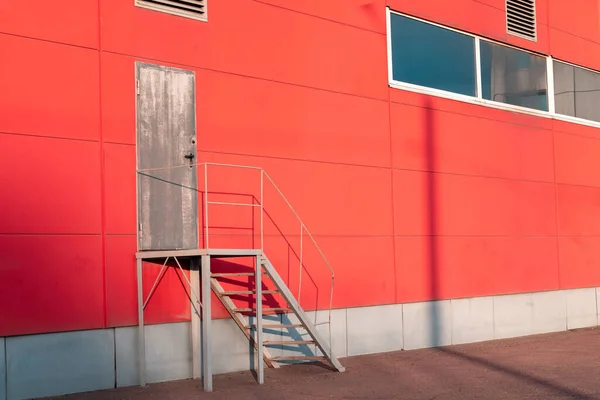 Emergency exit with metal stairs on the red facade of an industrial building, store, warehouse, logistics center. Iron staircase for up to maintenance work.