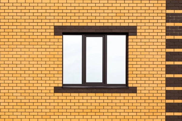 A three-pane window against a new brick wall. A fragment of a house wall for a construction-themed design. Clouds are reflected in the window. Copy space