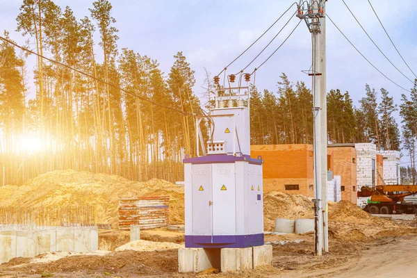 Gün batımında bir inşaat sahasında, yüksek voltaj direklerinin yanında, mobil canlı bir trafo kulübesi duruyor..