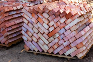 Tam gövdeli tuğlalarla dolu raflar. Birkaç palet kırmızı tuğla üst üste istiflenmiş. Tuğla işi için malzeme.