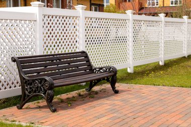 Köyde beyaz plastik bir çitin arkasındaki ahşap bank.