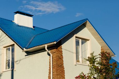 Bir evin çatısı ya da mavi metalden yapılma döşemeleri, lağımları, yamaçları, gelgitleri, mavi gökyüzüne karşı bacası olan bir kulübe. Çatı tasarımı için metal çatı, inşaat, mimari.