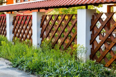 Özel bölgenin korunması için koyu renkli ahşap çitler. Çitin yanındaki uzun otlar.