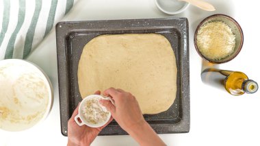 Peynirli ekmeği adım adım pişiriyorum. Ekmek hamuru bir yemek tepsisinde. Ekmek hamurunu tuzla kaplamak. Yakın çekim, üst görünüm, kadın eli, beyaz arka plan.