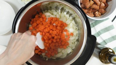 Saute chopped carrot and onion in a multi cooker. Cooking rice with meat and vegetables  in pressure multi cooker step by step, top view.