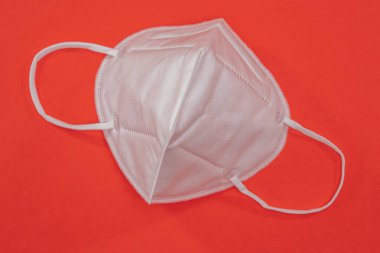 Kırmızı arka planda beyaz renkli bir tıbbi maske ve fotokopi alanı. Virüs ve salgın hastalığın yayılmasını önlemek için koruyucu ağız filtresi maskesi. Hastalıklar, grip, hava kirliliği, corona virüsü konsepti