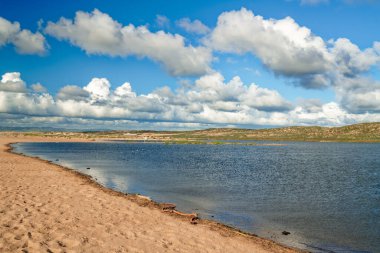 Tepeli kumlu göl kıyısı ve arka planda bulutlu gökyüzü