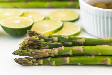 Yeşil kuşkonmaz, dilimlenmiş limon, zeytinyağı beyaz arka planda mermer servis tahtasına yakın.