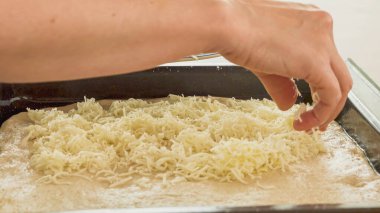 Pizza hamuru ya da ekmek hamuru ve rendelenmiş Mozzarella peyniri. Kadın hamur üstüne peynir koyuyor