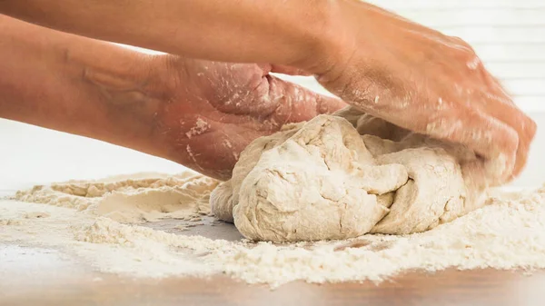 Bread dough or pizza dough close up on wooden kitchen table. Woman hands kneading whole wheat flour bread dough