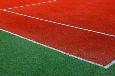 Part of empty used red tennis court playground surface with white lines closeup