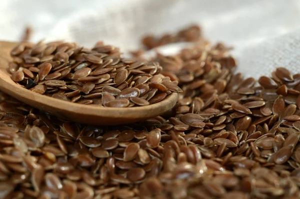 Chiuda semi di lino nel cucchiaio di legno su tessuto di lino — Foto Stock