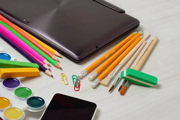 School or student supplies with closed slim notebook and smartphone on a white wooden table surface — Stock Photo, Image