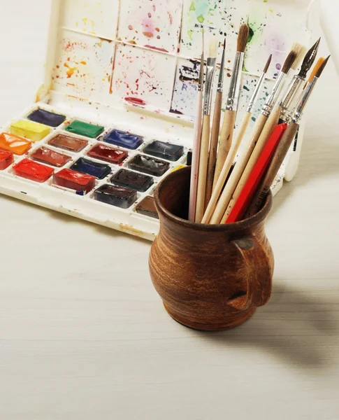 Pinturas de acuarela brillantes y pinceles usados para pintar sobre una superficie de mesa de madera. Vintage tonificado foto — Foto de Stock