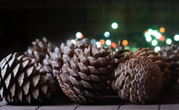 Weihnachtskarte mit Tannenzapfen und schönen Bokeh-Lichtern aus Girlanden auf hölzernem Hintergrund, rustikales Bild. Winterurlaub — Stockfoto