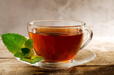 Bir fincan taze yeşil sulu nane yapraklı sıcak nane çayı. Eski ahşap bir arka planda, cam bir fincanda Aromatik çay.