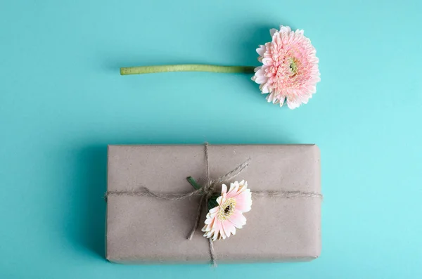 シンプルな茶色のクラフト紙に包まれた美しいギフトボックスには、パステルカラーの背景に生きたガーベラが飾られています。春のお祝いロマンチックなコンセプト. — ストック写真