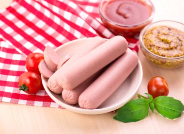 Çeri domatesli kaynamış süt sosisi, ketçap ve dijon hardalı ahşap bir masada..