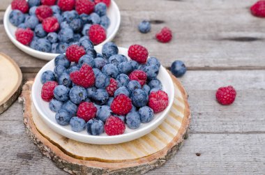 Bahçede, eski bir tahta masada yaban mersini ve ahududu ile natürmort. Kırsal doğal gıda tarzı.