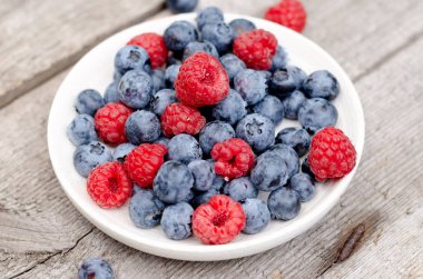 Bahçede, eski bir tahta masada yaban mersini ve ahududu ile natürmort. Kırsal doğal gıda tarzı.