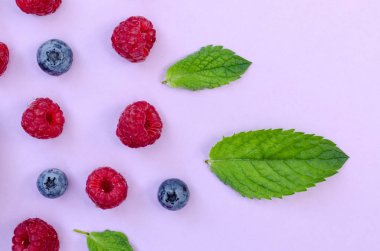 Pembe bir zemin üzerinde ahududu ve yaban mersinlerinin düz kompozisyonu ve süs olarak taze yeşil nane yaprakları..