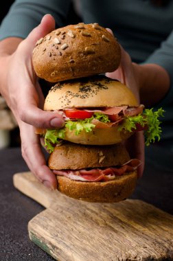Genç kadın elleri lezzetli çıtır hamburger ekmeği ve dilimlenmiş jambon tutuyor. Karanlık, karamsar yiyecekler..