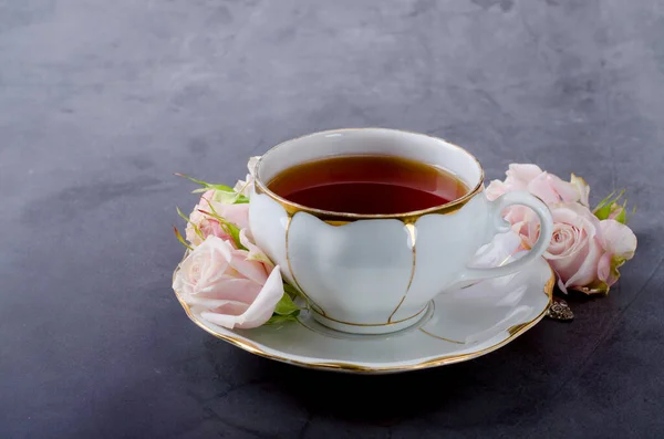 Beyaz porselen fincanlı çay saati, koyu gri arka planda yumuşak pembe güller.. — Stok fotoğraf