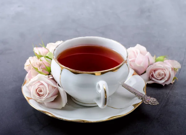 Tea time backdrop with vintage white porcelain tea cup, gentle pink roses on a dark gray background.