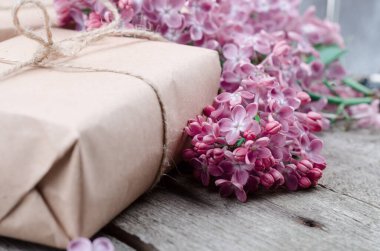 El yapımı, kahverengi kağıtlarla sarılı, eski ahşap bir yüzeyde taze mor leylak çiçekleriyle süslenmiş hediye kutuları. Bahar tatili geçmişi.