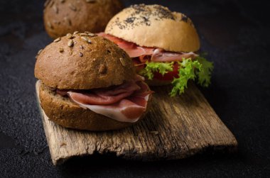 Kaliteli ahşap kesme tahtasının üzerinde dilimlenmiş jambonlu lezzetli çıtır burger ekmeği. Koyu karamsar yemek fotoğrafı bar menüsü ve posterleri için iyidir..