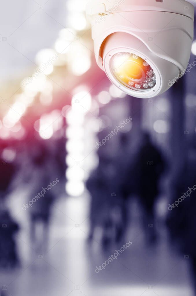 Cctv camera security system on a ceiling of a shopping mall blurred background. Toned image with light flare mock up