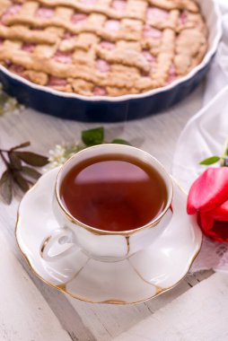 Beyaz porselen çay ve taze pişmiş turta. İngiliz kahvaltısı, içki ve ikramlar, kırmızı lale çiçeği ve beyaz masa örtüsü..