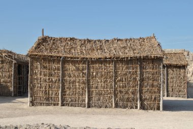  Güneşli bir günde Bahreyn Ulusal Şatosu 'nda el yapımı saman evler, Qal' at Al Bahreyn Kalesi
