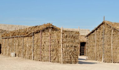  Güneşli bir günde Bahreyn Ulusal Şatosu 'nda el yapımı saman evler, Qal' at Al Bahreyn Kalesi
