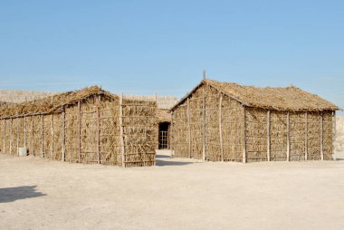  Güneşli bir günde Bahreyn Ulusal Şatosu 'nda el yapımı saman evler, Qal' at Al Bahreyn Kalesi