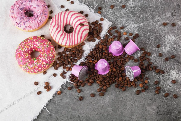 Espresso pembe plastik kapsüller folyo, kahve çekirdekleri ve gri beton arka planda tatlı çörekler.