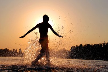 Çocuk suyun üzerinde koşuyor. Ayaklarını spreyliyor.