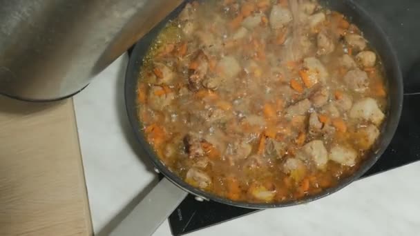 The cook pours the boiling water from the kettle to the beef roast for braising on low heat. — Stock Footage The cook pours the boiling water from the kettle to the beef roast for braising on low heat. Stock Video