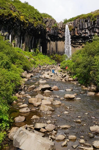 Azonosítatlan turisták elhelyezés egy sziklán, a Svartifoss, Izland. — Stock Fotó