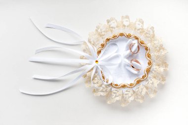 Altın alyanslar kuğularla süslenmiş dantel bir düğün yastığında. Beyaz arkaplanda yakın plan