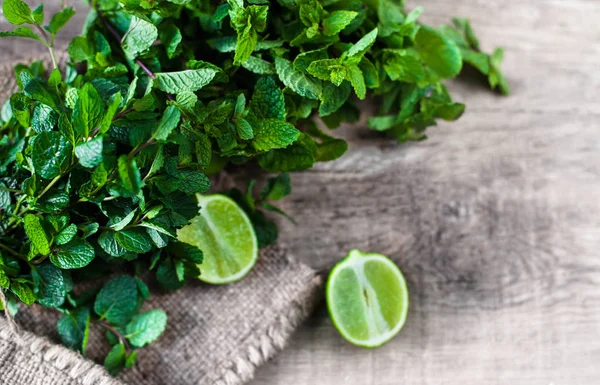 Menta fresca, limas, azúcar sobre fondo de madera — Foto de Stock