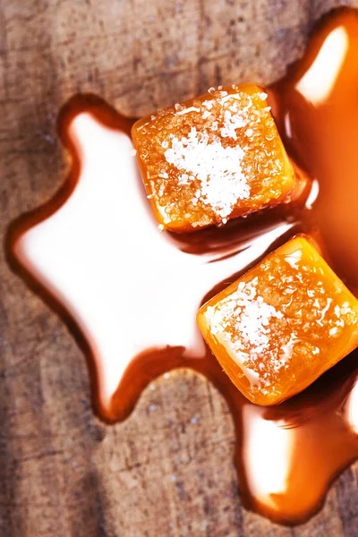 Homemade  Caramel sauce flowing on caramel candies on wooden  background. Golden Butterscotch toffee candy caramel