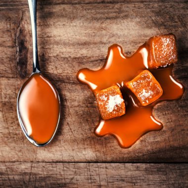 Ev yapımı tuzlu karamel adet ahşap arka plan üzerinde. Altın karamela toffee şeker karamel ile boşaltmak