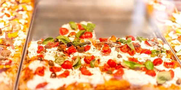 Pizza Take Away pieces on a stall in pizzeria in Italy,  Traditional Italian Focaccia with tomatoes, black olives and chees